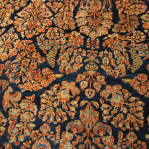 Close-up of a dark blue rug with a dense all-over pattern of orange and gold stylized florals.