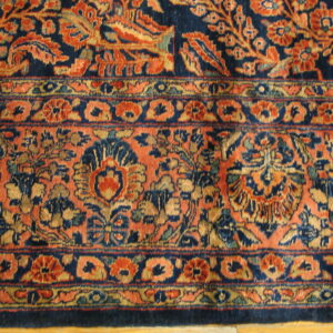 Detail shot showing a medium-pile rug border and field with complex navy, rust, and gold floral designs.