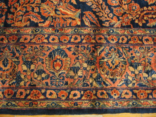 Detail shot showing a medium-pile rug border and field with complex navy, rust, and gold floral designs.