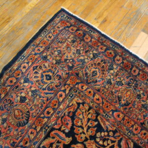 Blue and salmon ornate rug corner with multiple borders resting on distressed golden hardwood flooring.