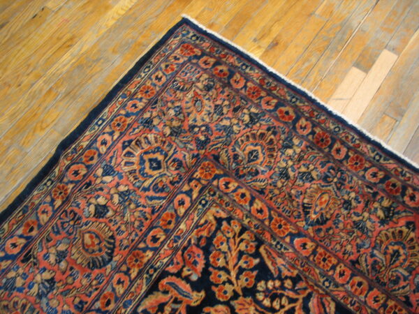 Blue and salmon ornate rug corner with multiple borders resting on distressed golden hardwood flooring.