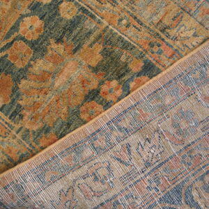 Traditional rug with teal, rust, and gold floral patterns, partially folded to reveal the woven backing.