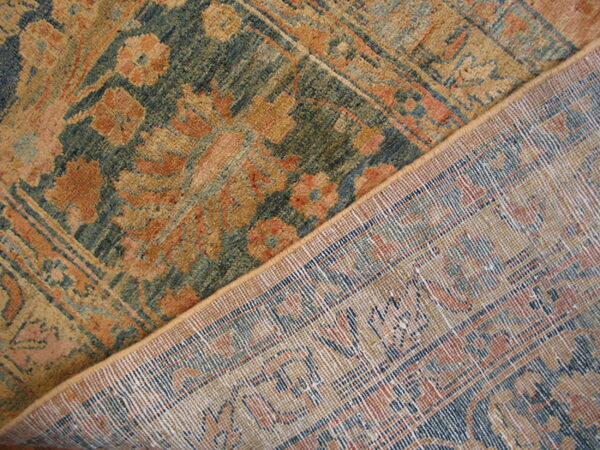Traditional rug with teal, rust, and gold floral patterns, partially folded to reveal the woven backing.
