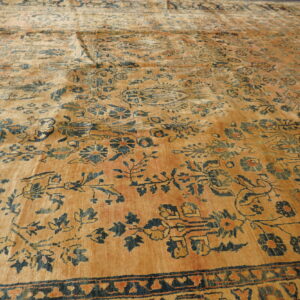 Angled view of a low-pile saffron rug featuring a complex dark blue and rust botanical pattern.