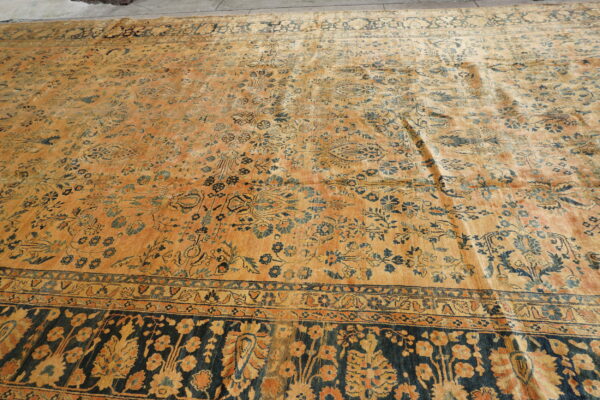 Large orange and blue low-pile rug with a dense floral pattern and wide dark border on concrete flooring.