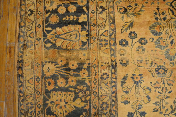 Ornate yellow and charcoal rug with floral motifs and geometric borders lies on distressed plank wood flooring.