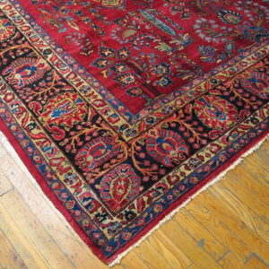 Red patterned rug featuring dark blue and gold floral borders on light brown hardwood flooring.
