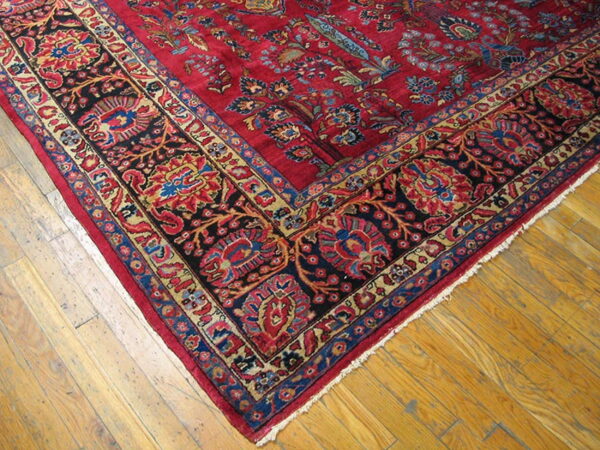Red patterned rug featuring dark blue and gold floral borders on light brown hardwood flooring.