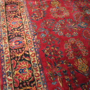 Close view of a red floral rug with a contrasting black border on golden hardwood floors.