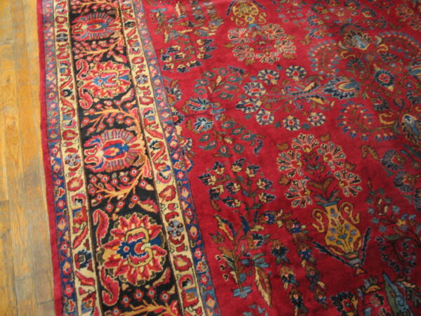 Close view of a red floral rug with a contrasting black border on golden hardwood floors.