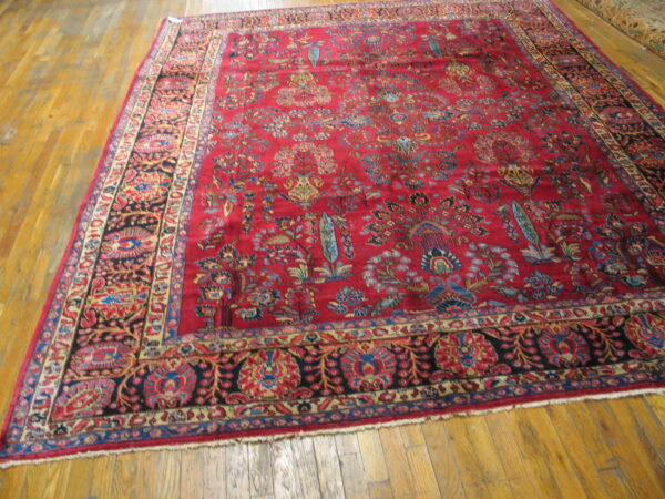 A large, deep red rug with dense floral and bird motifs covers a glossy plank wood floor.