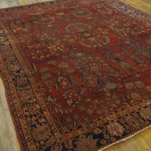 Rust-red rug with an elaborate navy and gold floral pattern displayed on a light wood floor.