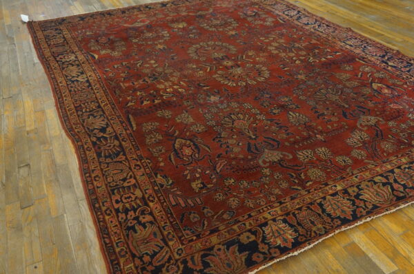 Rust-red rug with an elaborate navy and gold floral pattern displayed on a light wood floor.