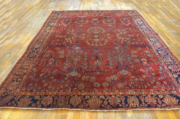 Intricately patterned red rug featuring navy and gold botanical designs lies on light hardwood planks.