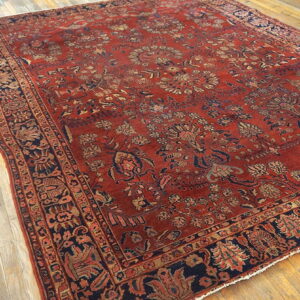Rust-toned area rug featuring detailed blue and beige floral patterns lying on a natural wood floor.
