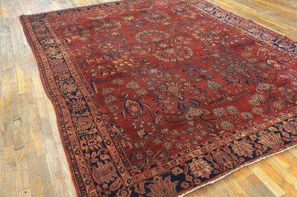 Rust-toned area rug featuring detailed blue and beige floral patterns lying on a natural wood floor.