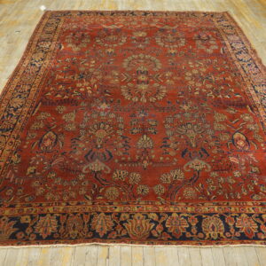 Large red rug with dense floral patterns in navy and gold, resting on worn wooden floors.