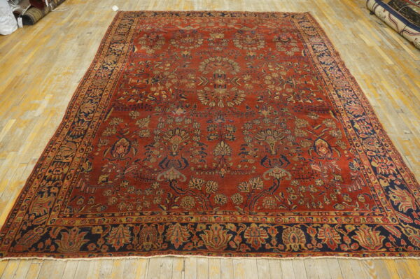 Large red rug with dense floral patterns in navy and gold, resting on worn wooden floors.