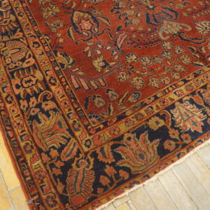 Low-pile rug in deep red, navy blue, and gold floral patterns rests on distressed light wooden plank flooring.