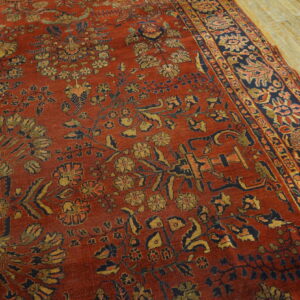 Rust-colored rug with intricate gold and navy floral motifs rests on light, visible wooden planks.