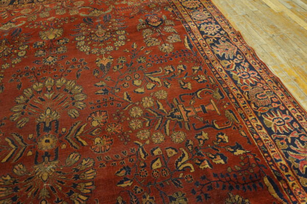 Rust-colored rug with intricate gold and navy floral motifs rests on light, visible wooden planks.