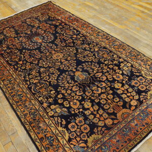 Navy rug with a dense orange and gold botanical pattern sits on angled light hardwood flooring.