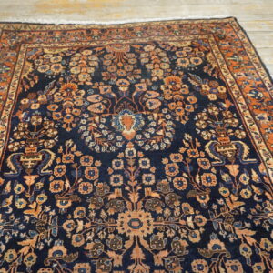 Navy blue rug featuring a dense floral pattern in rust and peach tones on light wood flooring.