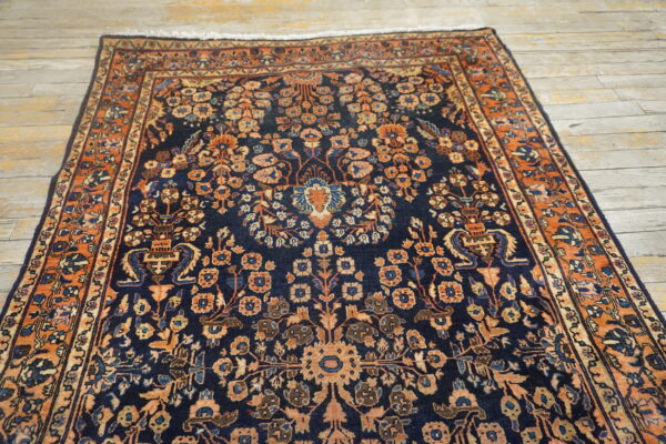 Navy blue rug featuring a dense floral pattern in rust and peach tones on light wood flooring.