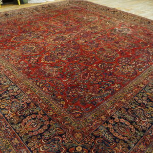 Ornate red and navy traditional rug with gold and blue accents covers light distressed wooden plank flooring.