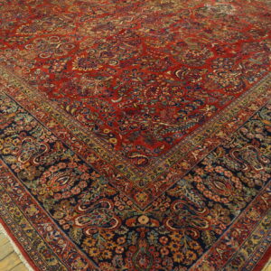 Detailed red rug with dense floral patterns and a navy border on rustic wood planks.