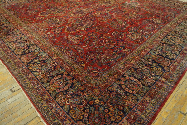 Detailed red rug with dense floral patterns and a navy border on rustic wood planks.