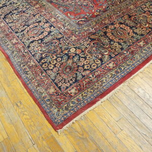 Traditional navy rug with red and gold floral designs lies diagonally on distressed wooden planks.