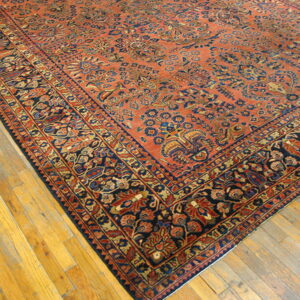 A traditional rug with an orange field and elaborate navy floral border rests on light wood plank flooring.