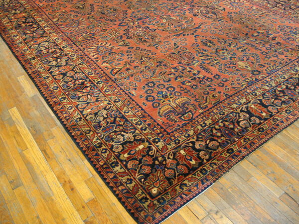A traditional rug with an orange field and elaborate navy floral border rests on light wood plank flooring.