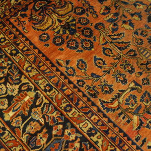 Ornate rug detail showing a rust-orange field and a dark border filled with blue and gold floral motifs.