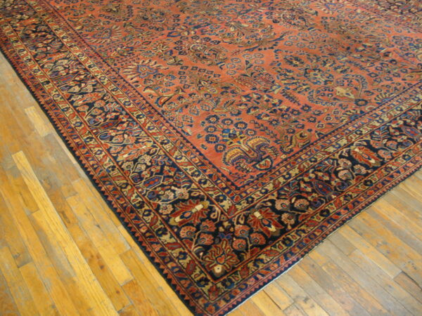 Ornate rust and blue floral rug with a wide navy border covers light golden hardwood planks.