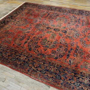 A rust-colored traditional rug with navy and gold floral patterns lies on weathered gray wood floorboards.