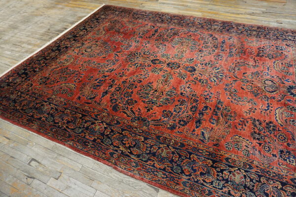A rust-colored traditional rug with navy and gold floral patterns lies on weathered gray wood floorboards.