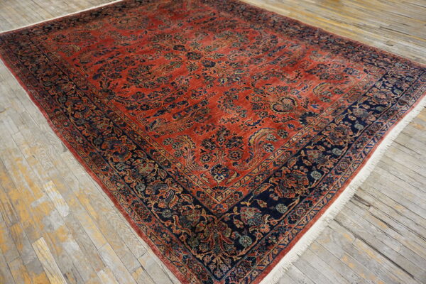 Intricate rust and navy rug with floral motifs and low pile rests on weathered wood planks.