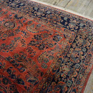 Detailed navy and coral traditional rug with floral motifs lying on gray plank wood flooring.
