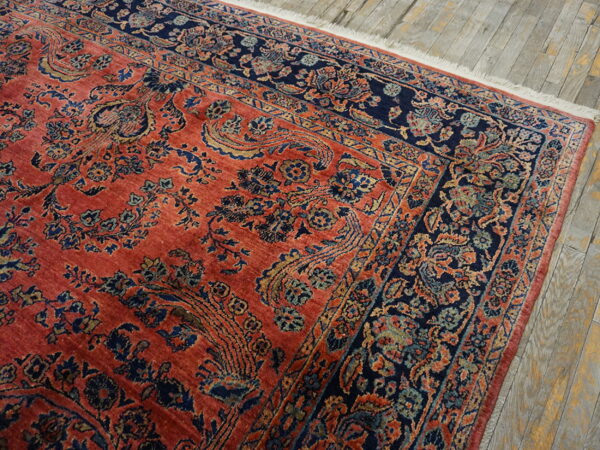 Detailed navy and coral traditional rug with floral motifs lying on gray plank wood flooring.