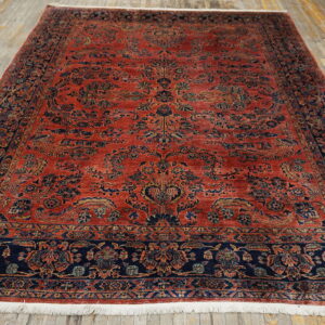 Intricate floral rug in deep red and navy blue with short fringe on light wood planks.