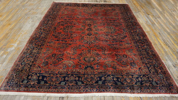 Intricate floral rug in deep red and navy blue with short fringe on light wood planks.
