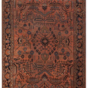 Rust colored rug with intricate dark navy borders and a central field of geometric and stylized floral patterns.
