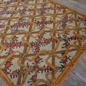A classical rug displaying a repeating pattern of gold ribbons and red roses on distressed hardwood.