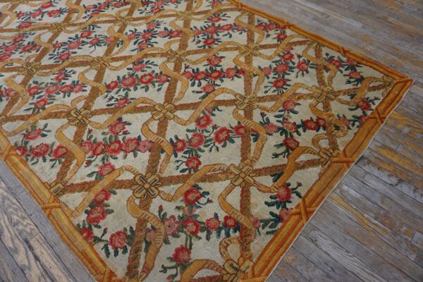 A classical rug displaying a repeating pattern of gold ribbons and red roses on distressed hardwood.