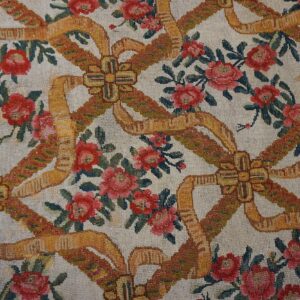 Ivory rug with red roses and golden ribbon bows sits beside rustic wood plank flooring.
