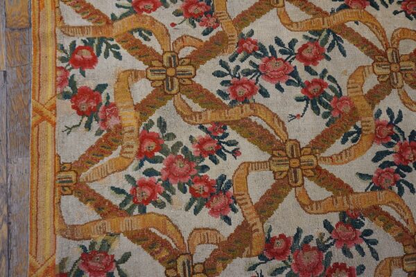 Ivory rug with red roses and golden ribbon bows sits beside rustic wood plank flooring.