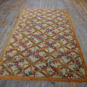 Cream rug with repeating gold ribbon trellis and red floral clusters on worn wood flooring.