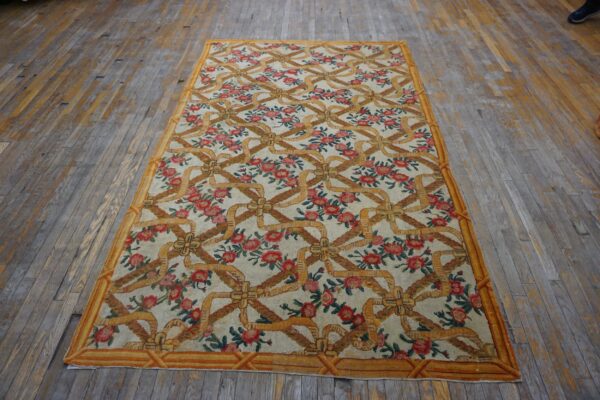 Cream rug with repeating gold ribbon trellis and red floral clusters on worn wood flooring.
